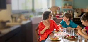 A mother and her two children sharing a meal together at the kitchen table